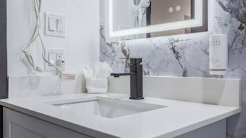 A modern bathroom with a white sink, a black faucet, a towel dispenser, and a hand soap bottle.