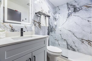 Uma casa de banho moderna com painel de parede em mármore, uma sanita e uma pia branca.
