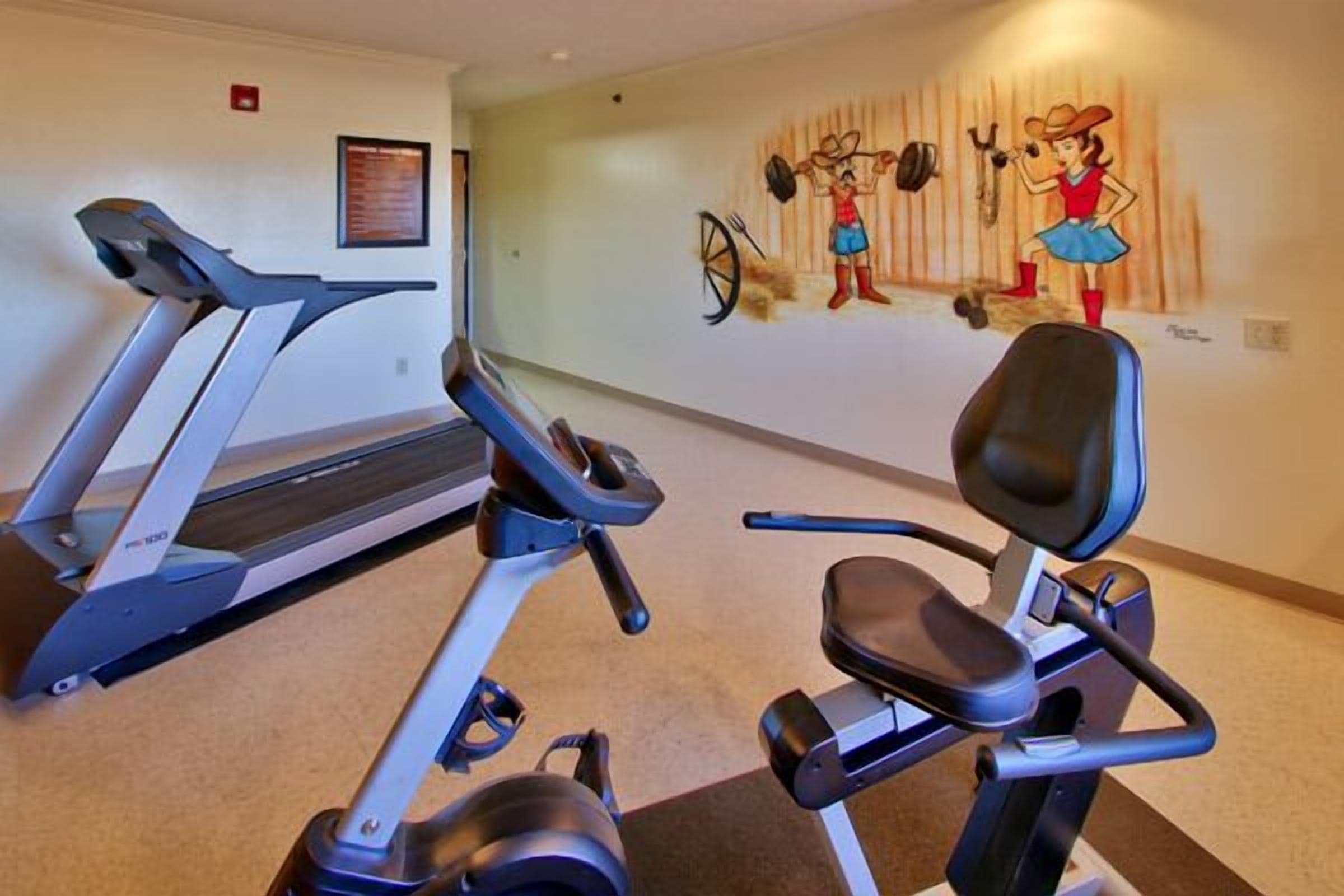 Ett gym med löpband och en motionscykel, en väggmålning och en inramad skylt.