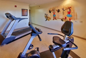 Un gimnasio con cintas de correr y una bicicleta estática, un mural en la pared y un cartel enmarcado.