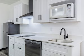 A modern kitchen with white cabinetry, a built-in microwave, a stainless steel sink, and a dishwasher. - Western Skies Inn And Suites (Los Lunas)