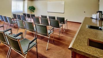 Une salle de conférence avec des rangées de chaises, un tableau blanc et un coin cuisine.