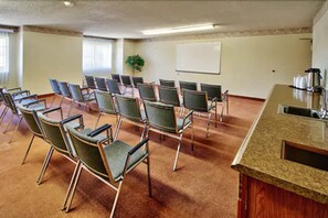 A conference room with rows of chairs, a whiteboard, and a kitchenette area. - Western Skies Inn And Suites (Los Lunas)