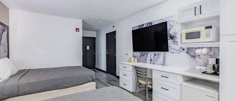 Een moderne slaapkamer met een bed, een bureau, een stoel, een flatscreen-tv en een magnetron.