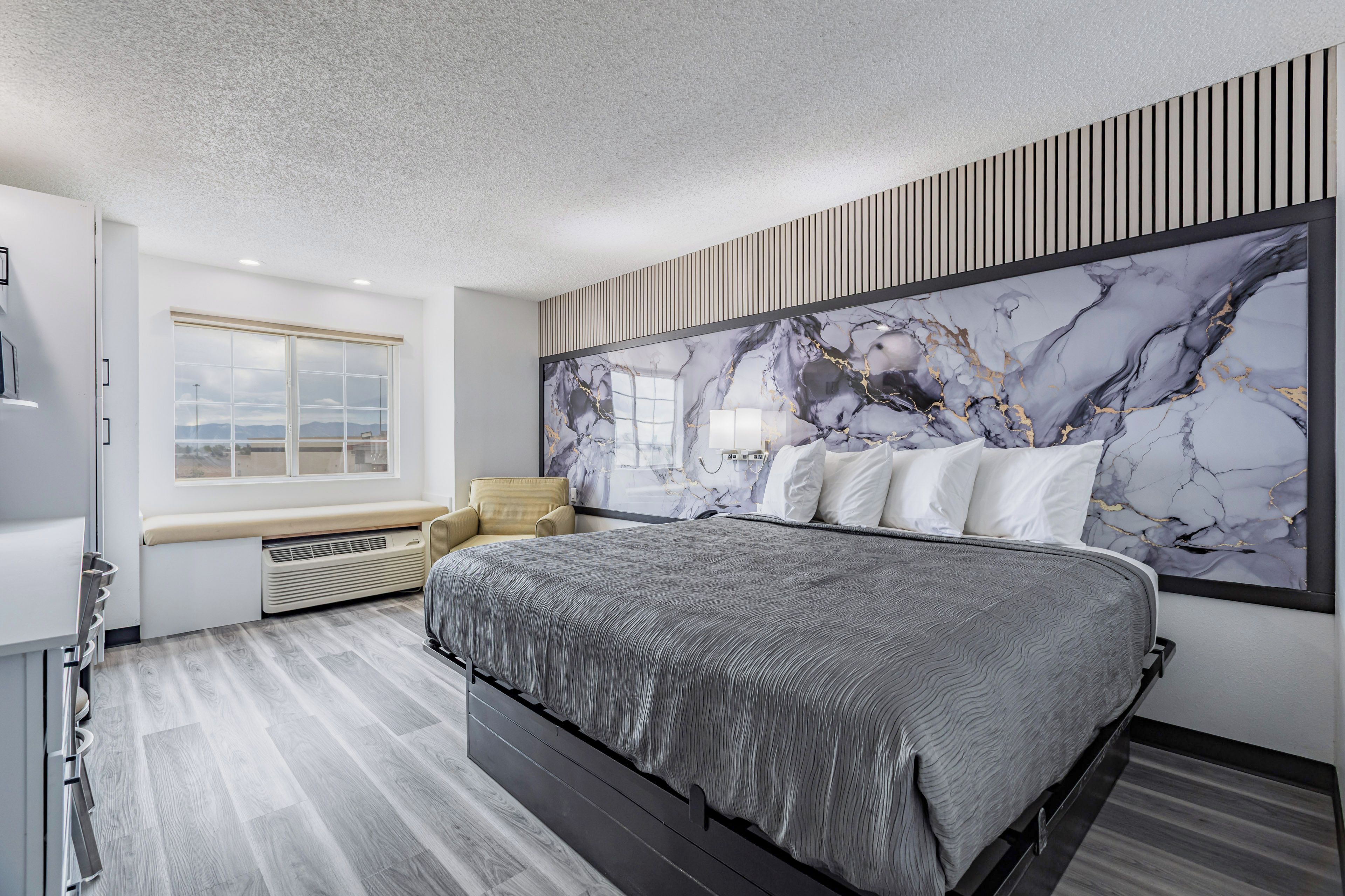 Une chambre moderne avec un grand lit, une fenêtre offrant une belle vue et une œuvre d’art en marbre ornant un mur.