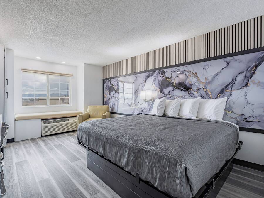 A modern bedroom with a large bed, a window with a view, and a marble wall art piece.