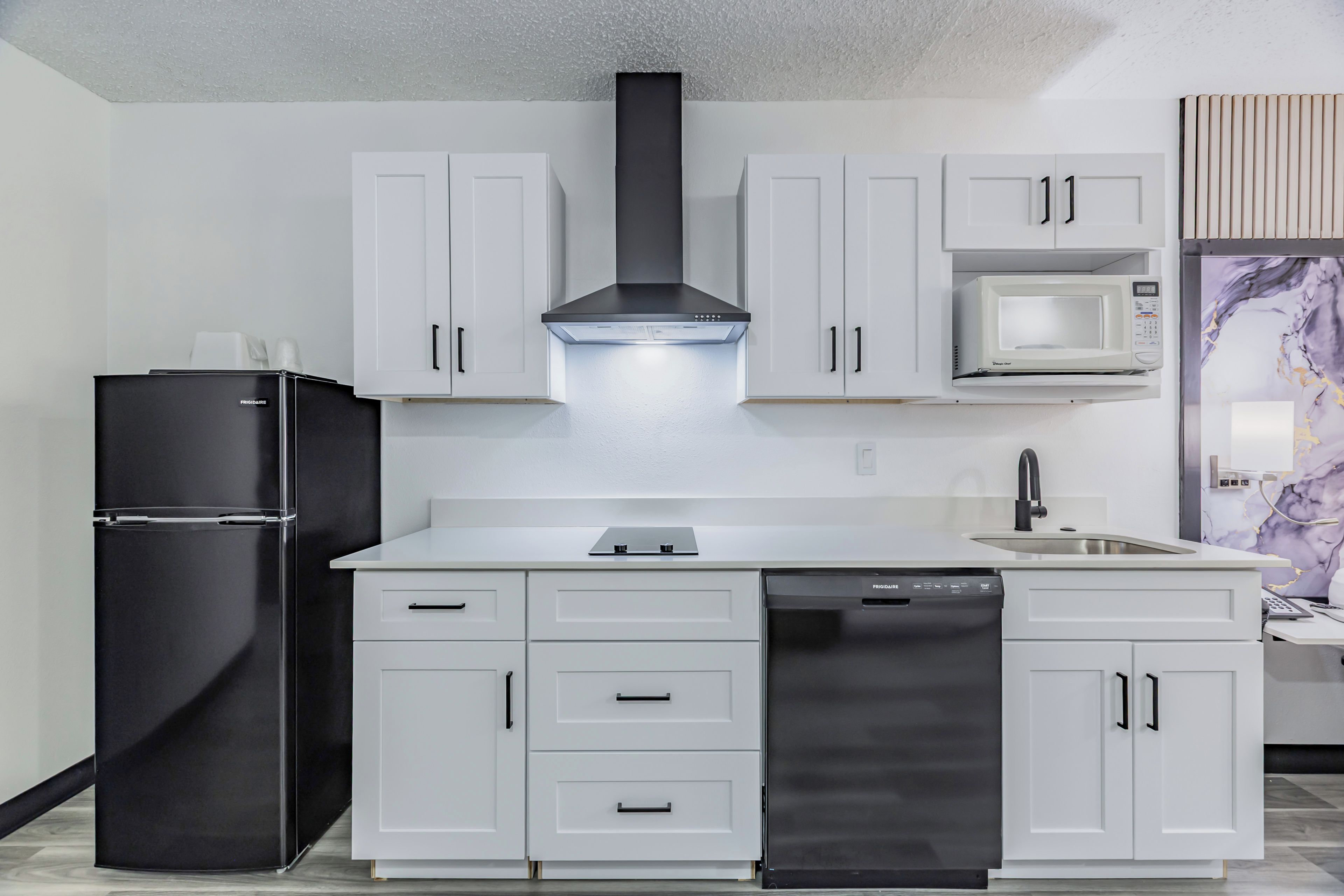 Una cocina moderna con armarios blancos, un refrigerador negro, un lavavajillas de acero inoxidable y un microondas.
