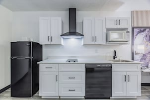 A modern kitchen with white cabinetry, a black refrigerator, a stainless steel dishwasher, and a microwave.