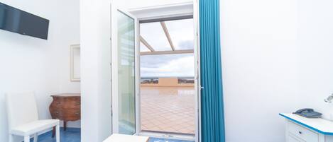 A room with a bed, a desk, a chair, a television, and a sliding glass door to an outdoor area.