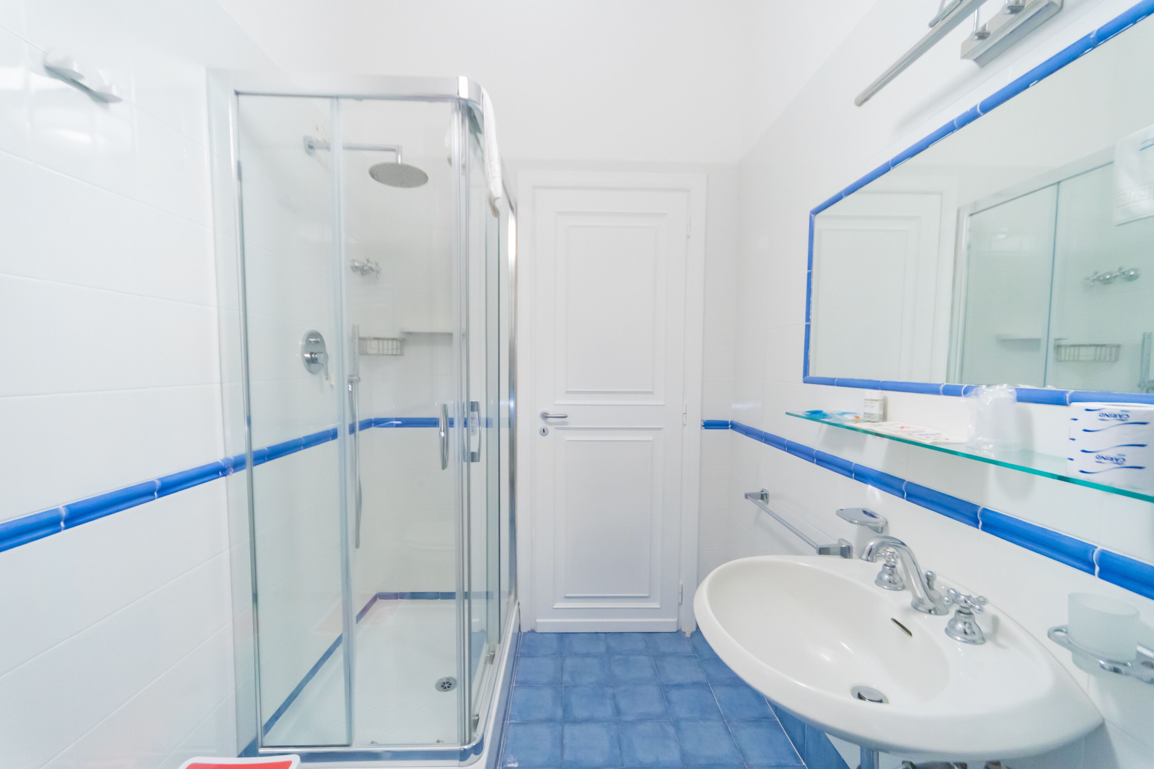 A bathroom with a glass shower enclosure, a white sink, and a large mirror.