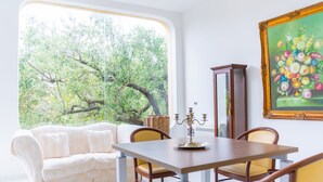 A room with a large window, a dining table with chairs, a sofa, and a painting on the wall. - Hotel America (Camerota)