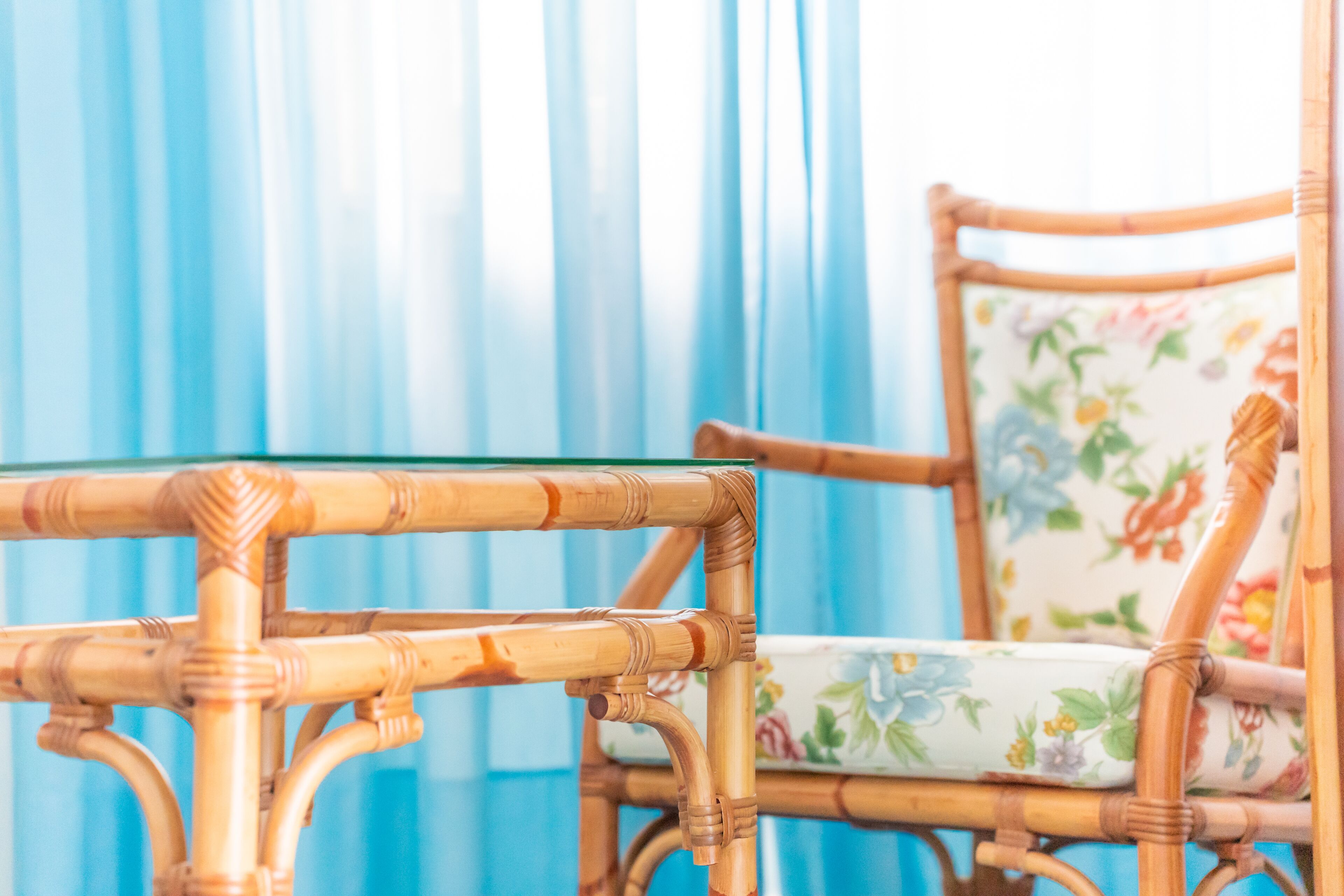 Una silla de mimbre con un cojín estampado y una mesa de vidrio al frente.
