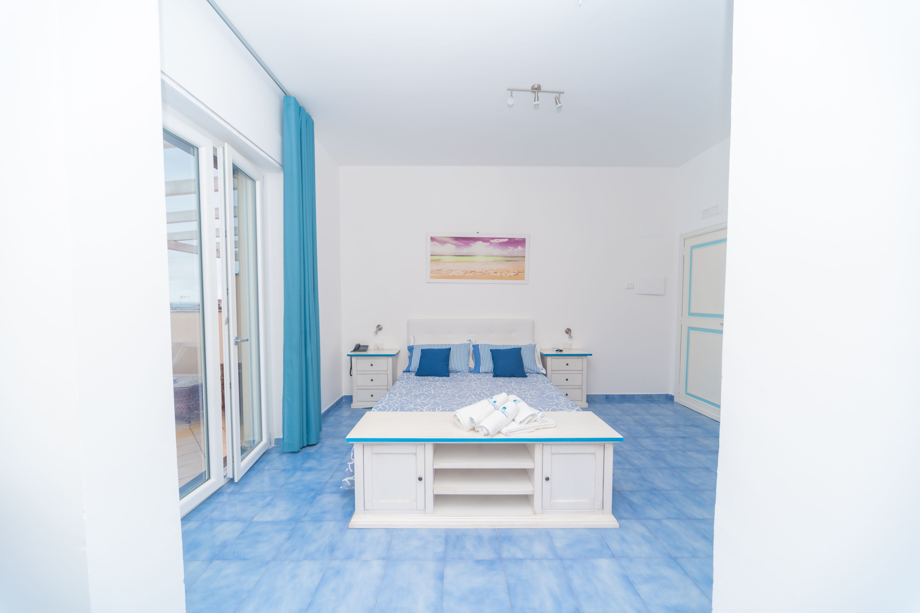 Ein Schlafzimmer mit einem Bett, einem Nachttisch, einem Tischchen, einem Bild an der Wand und einer Schiebeglastür.