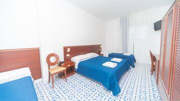 A hotel room with two beds, a wooden headboard, a chair, a small table, and a window with curtains.