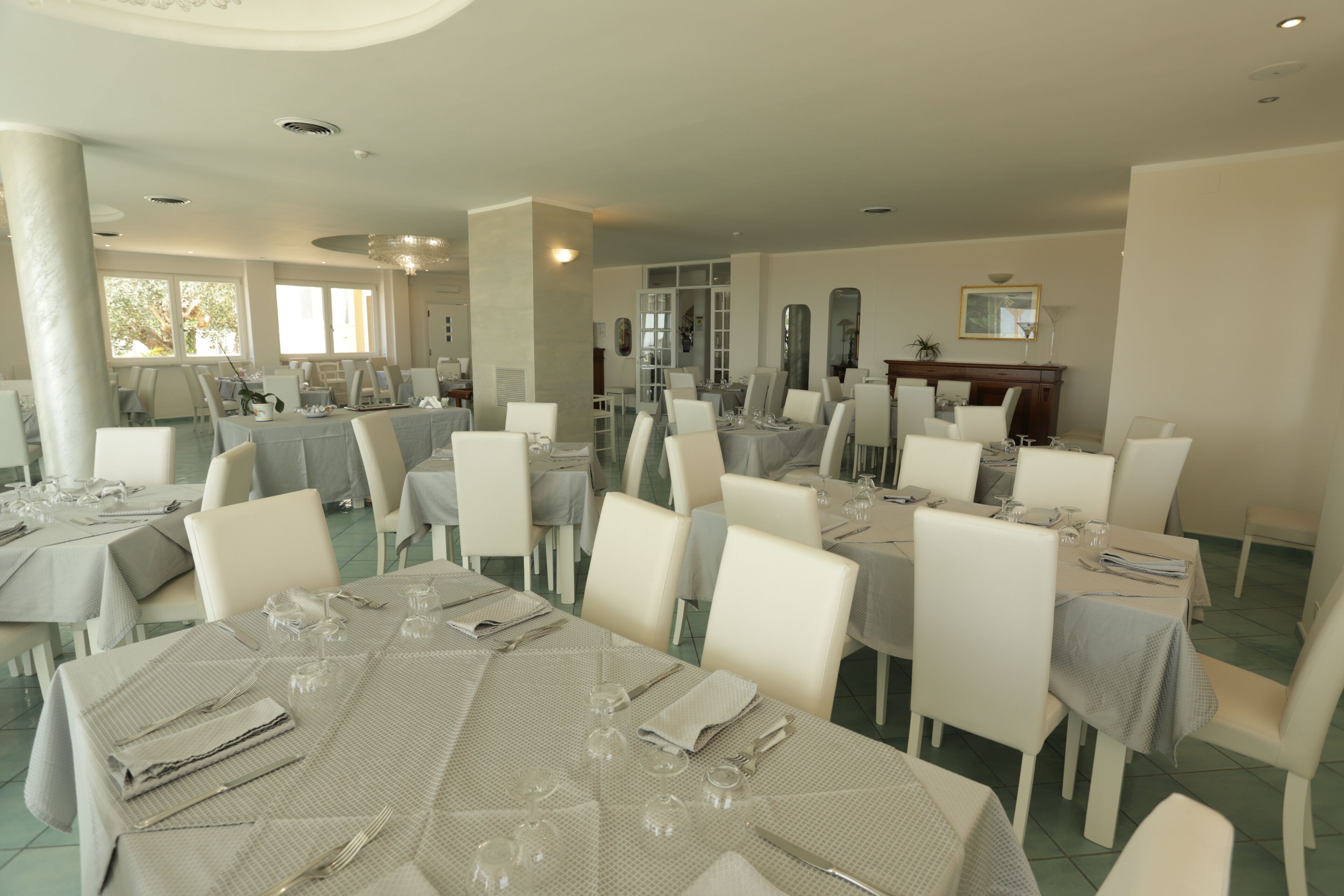 Un comedor espacioso con varias mesas dispuestas para recibir a los huéspedes, con sillas blancas y una presentación de mesa impecable.