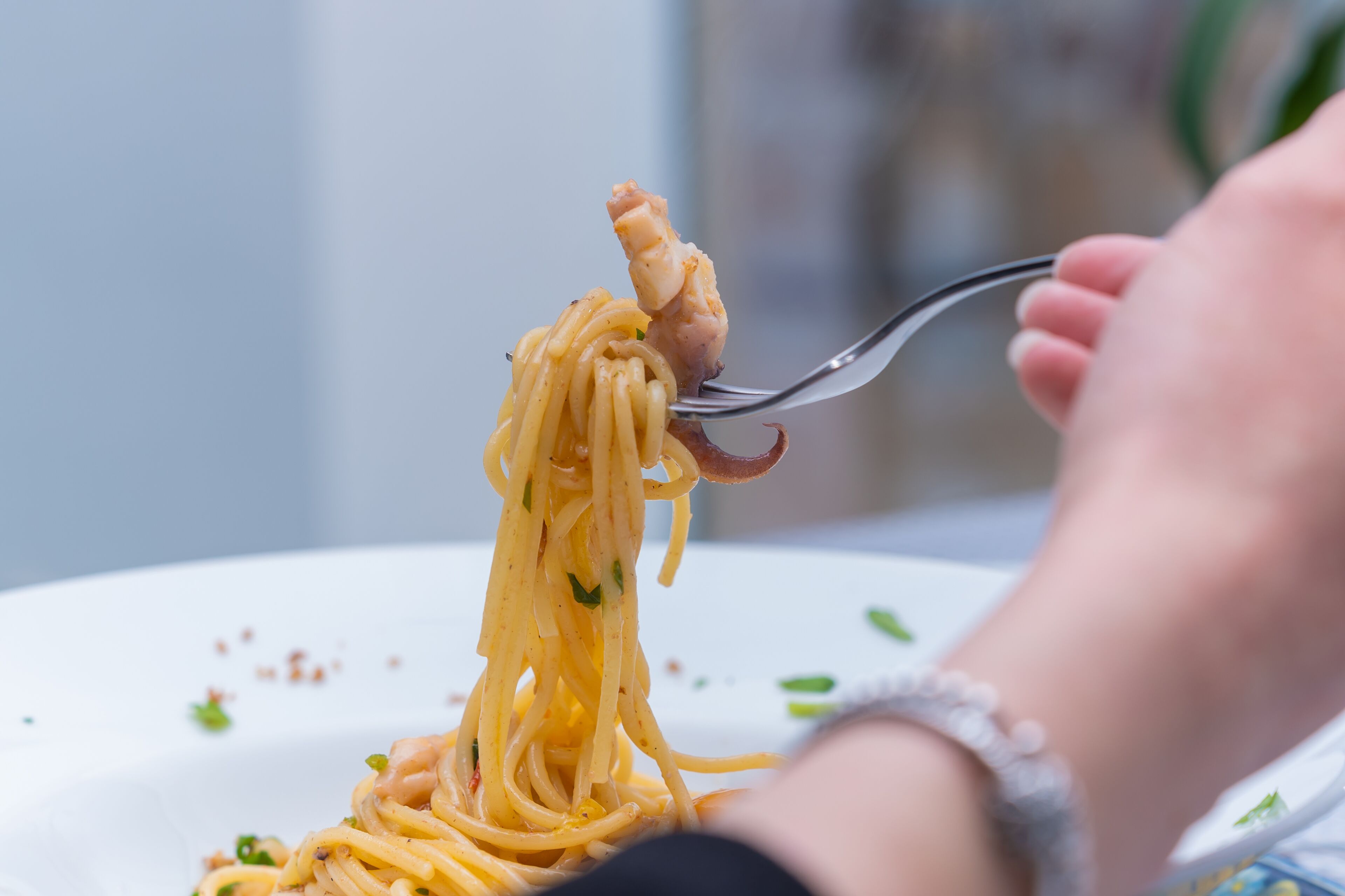 Primer plano de un tenedor levantando espagueti con un trozo de carne, sostenido por una persona que lleva una pulsera.