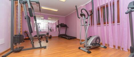 Un gimnasio con equipo de ejercicio, piso de madera y cortinas rosas.