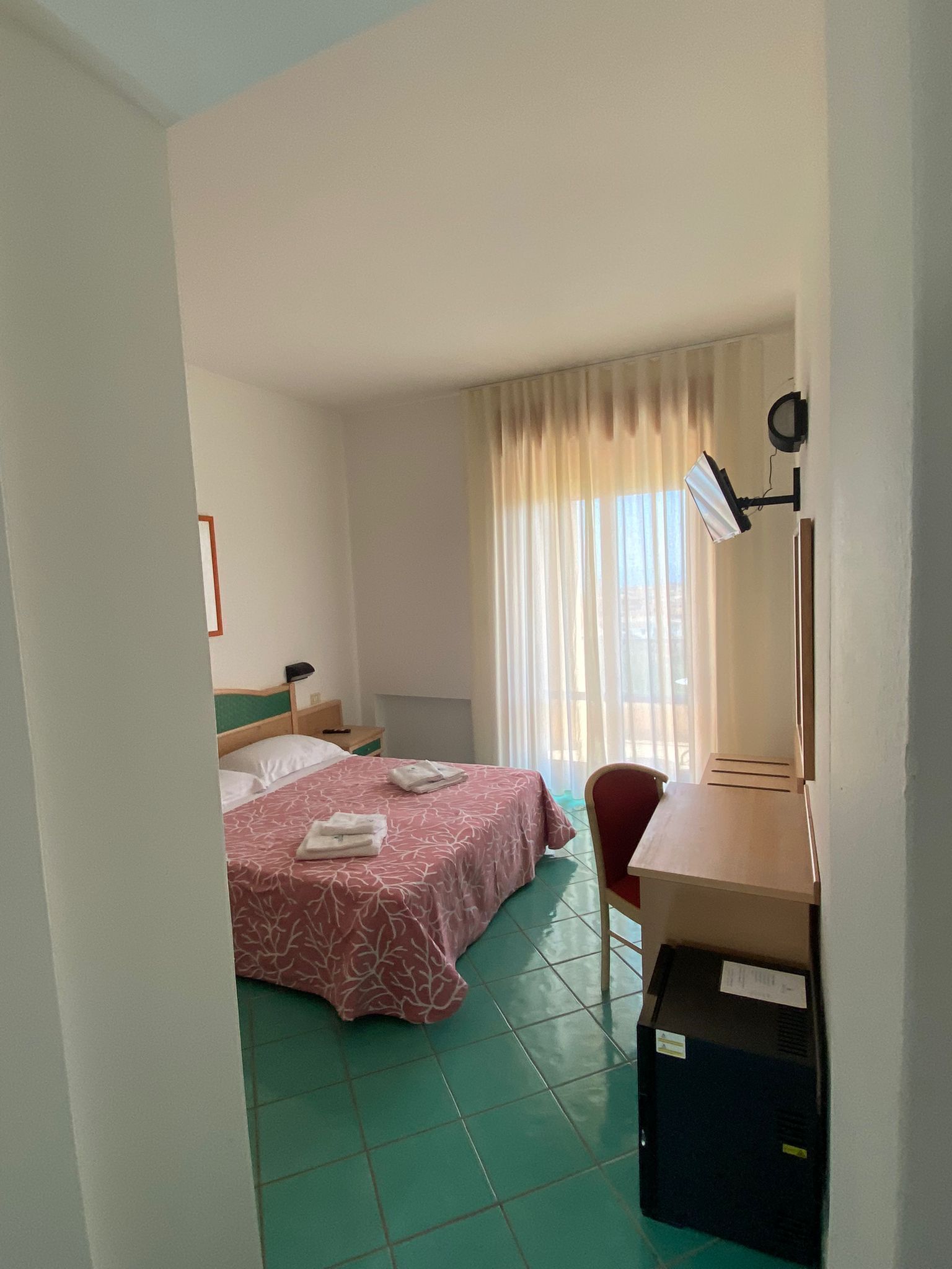Una habitación de hotel con una cama, un escritorio, una silla, una lámpara de escritorio y una ventana con cortinas.