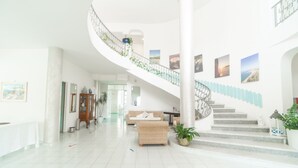 A spacious lobby with a spiral staircase, a sofa, and a potted plant. - Hotel America (Camerota)