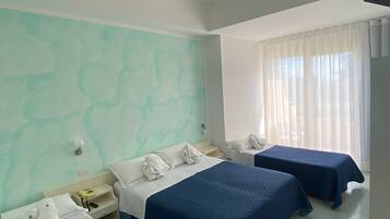 A hotel room with three beds, a window with sheer curtains, and a ceiling light fixture.