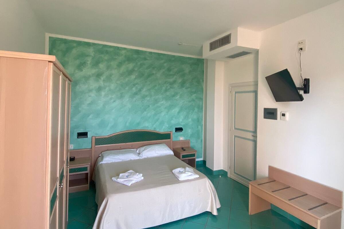 A bedroom with a bed, bedside tables, a wardrobe, a bench, and a wall-mounted TV.