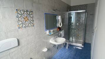 A bathroom with grey tiled walls, a blue-tiled floor, a white toilet, two sinks, a shower enclosure, and a decorative tile on the wall.