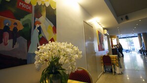 A hotel lobby with a modern art piece, a vase with white flowers, and a reception desk. - Cristal Palace Hotel (Buenos Aires)