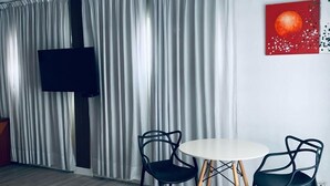 A modern living room with a round table and two chairs, a flat-screen TV mounted on the wall, and a large window with sheer curtains. - Cristal Palace Hotel (Buenos Aires)
