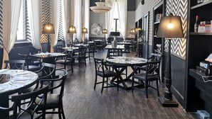 A restaurant with multiple round tables and chairs, large windows with curtains, and a zigzag patterned wall. - TH Roma - Carpegna Palace (Rome)