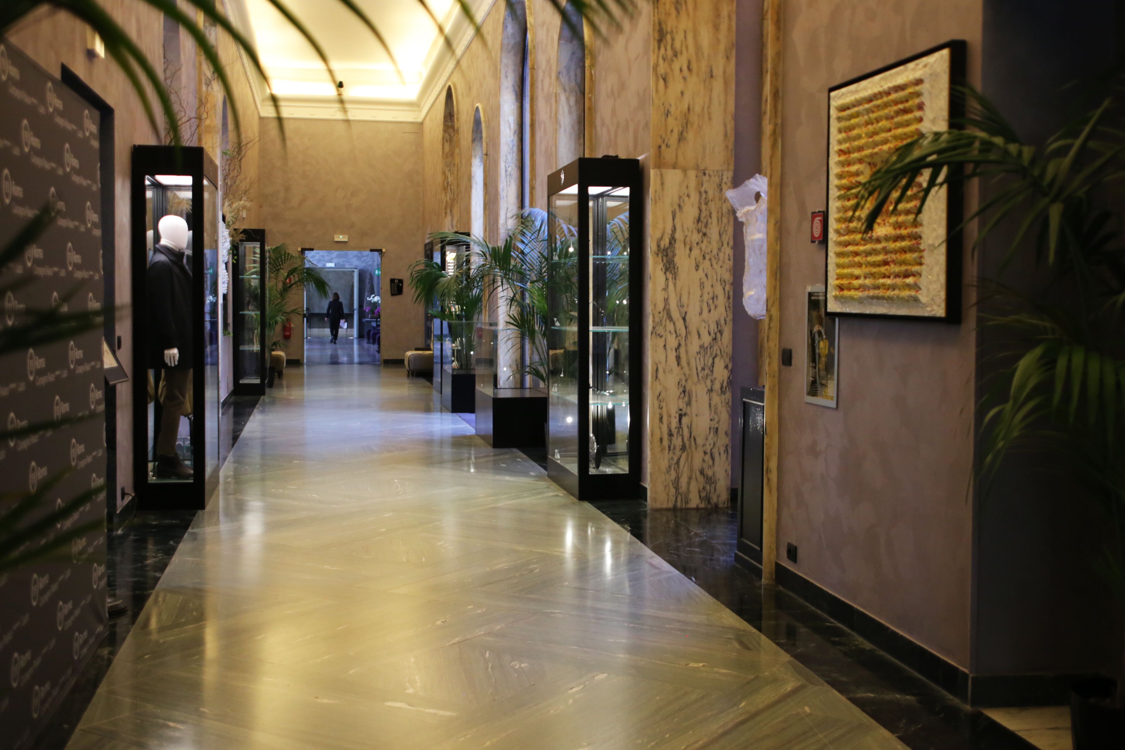 Un long couloir élégant, doté de sols en marbre, de portes d’ascenseur en verre et de plantes en pot.