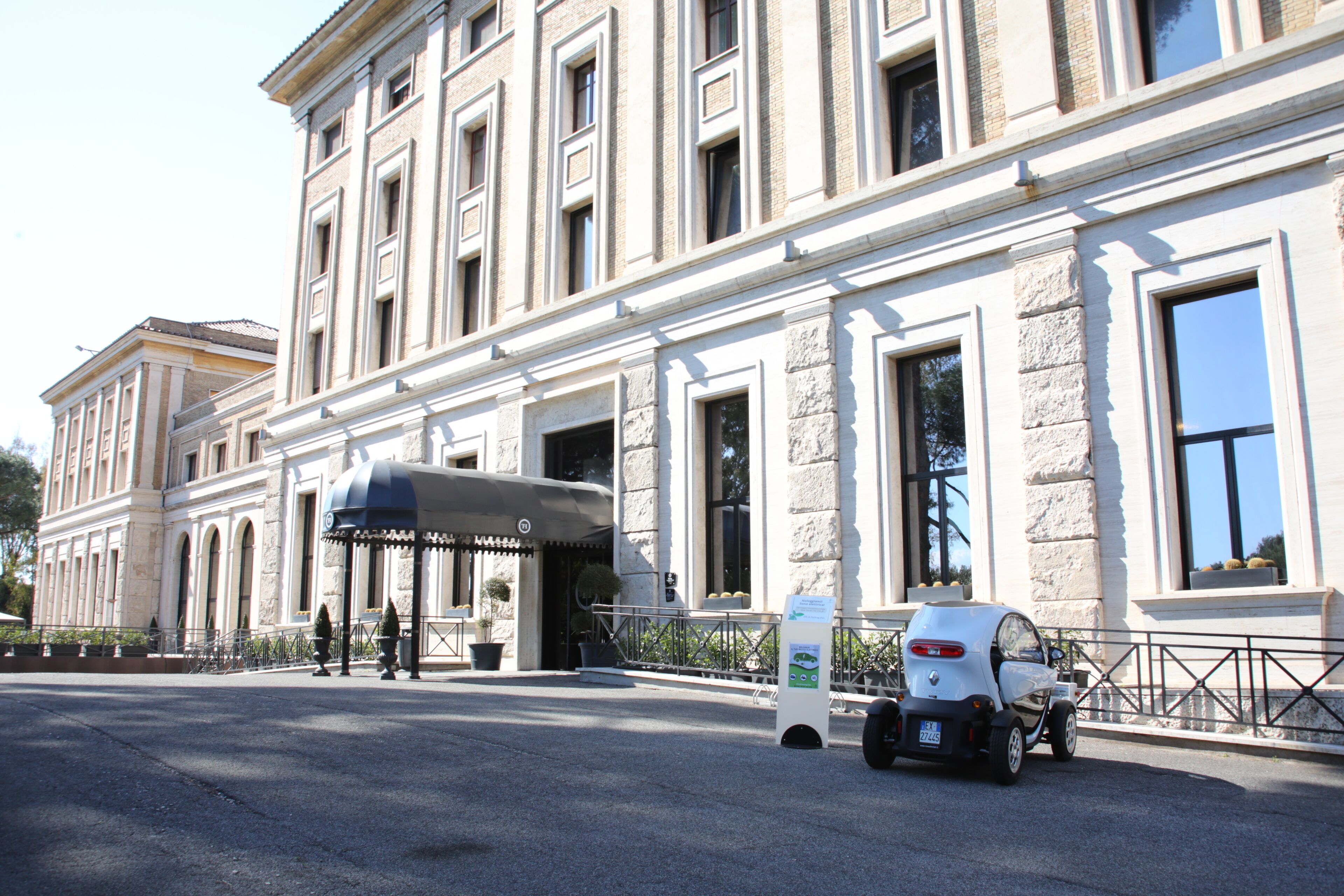 A historic building with a covered entrance, a parking area, and a small electric vehicle charging station.