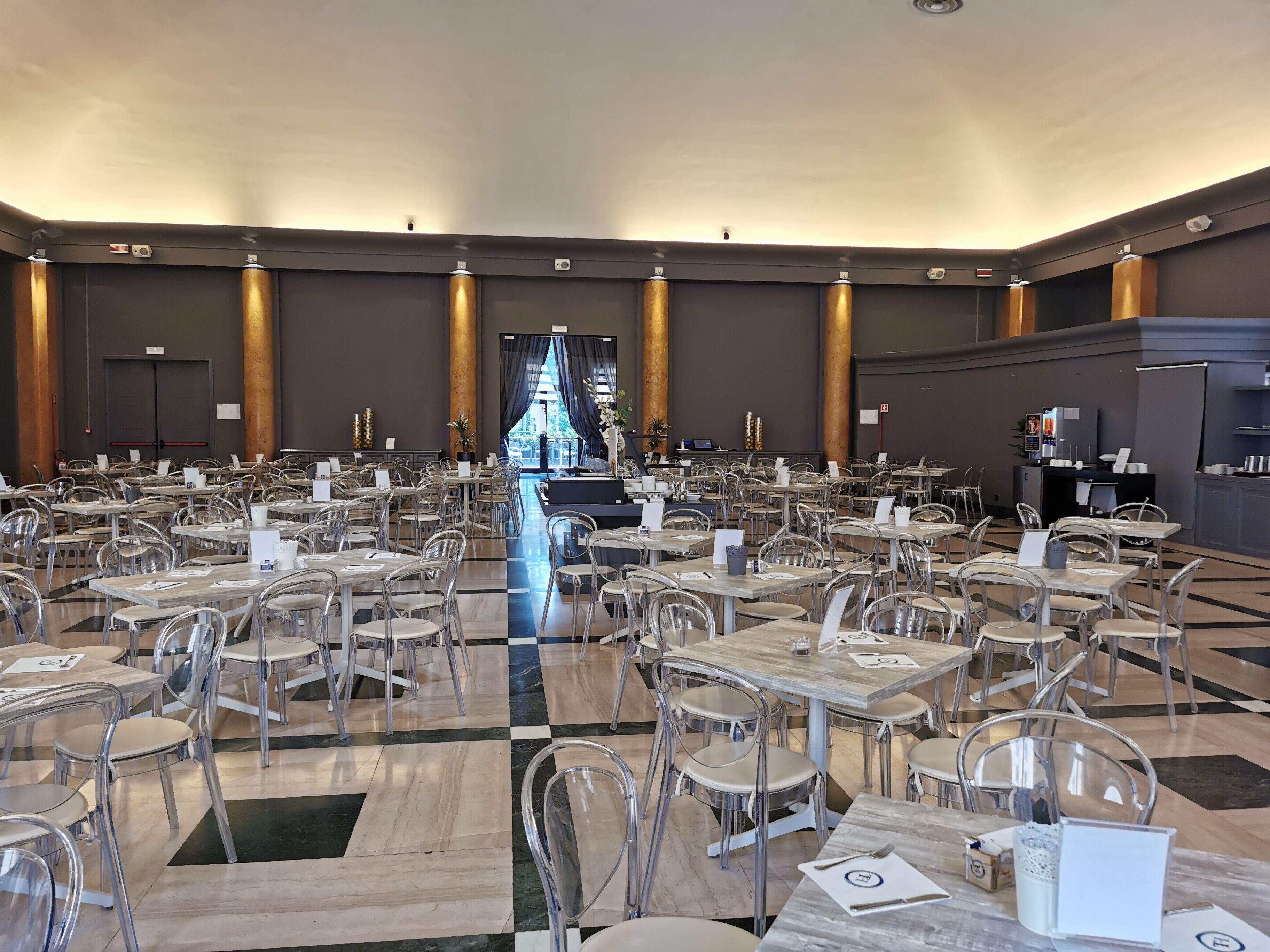 A spacious dining area with numerous tables and chairs, a central stage, and a kitchen area in the background.