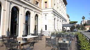 An outdoor cafe with tables and chairs, a fountain, and a building with arched windows. - TH Roma - Carpegna Palace (Rome)