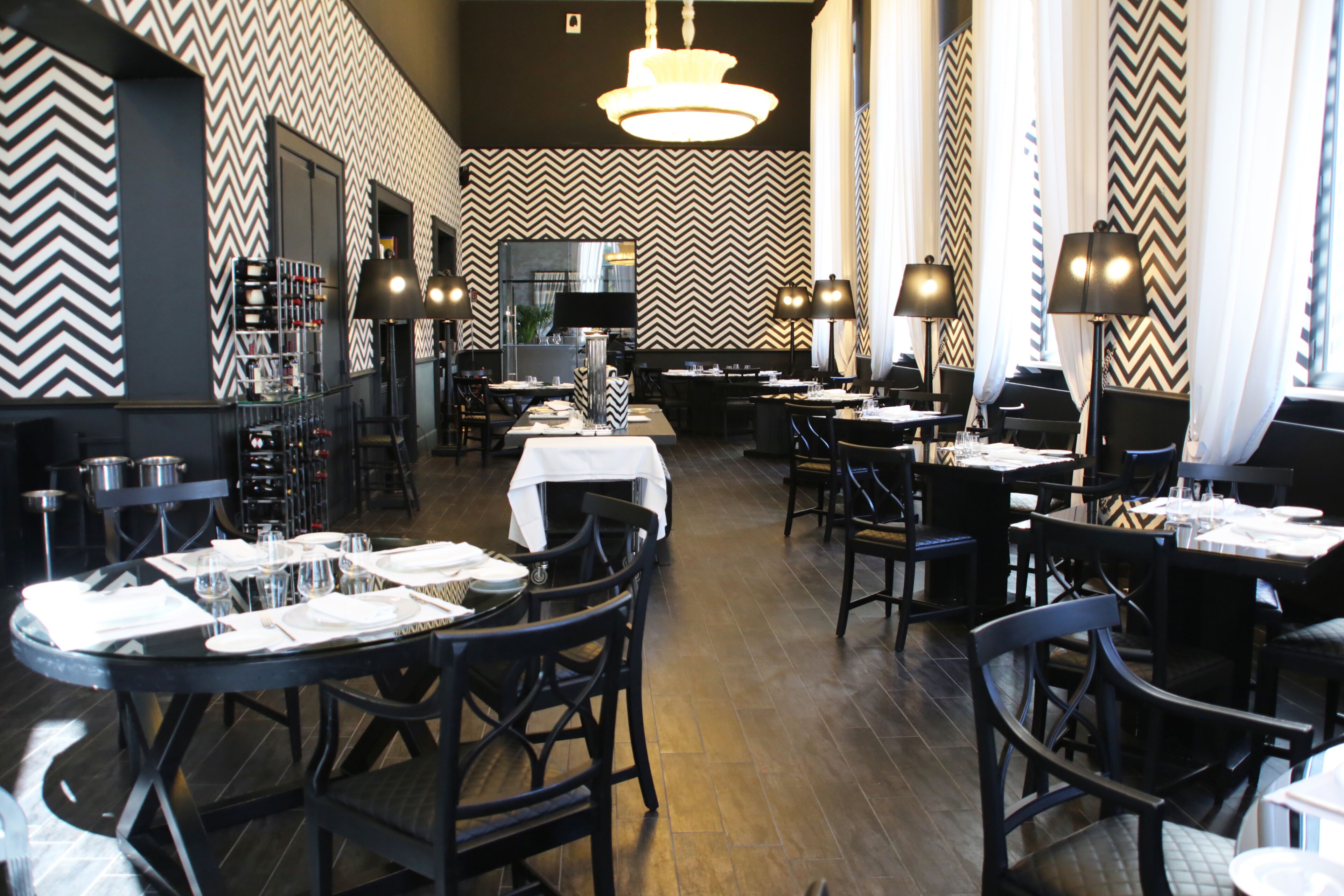 A restaurant with a zigzag patterned wall, black and white chairs, and tables set for dining.