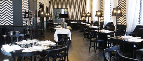 A restaurant with a zigzag patterned wall, black and white chairs, and tables set for dining.