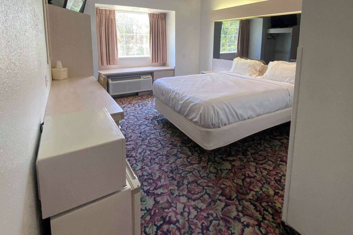 A hotel room with a bed, a desk, and a window with curtains.