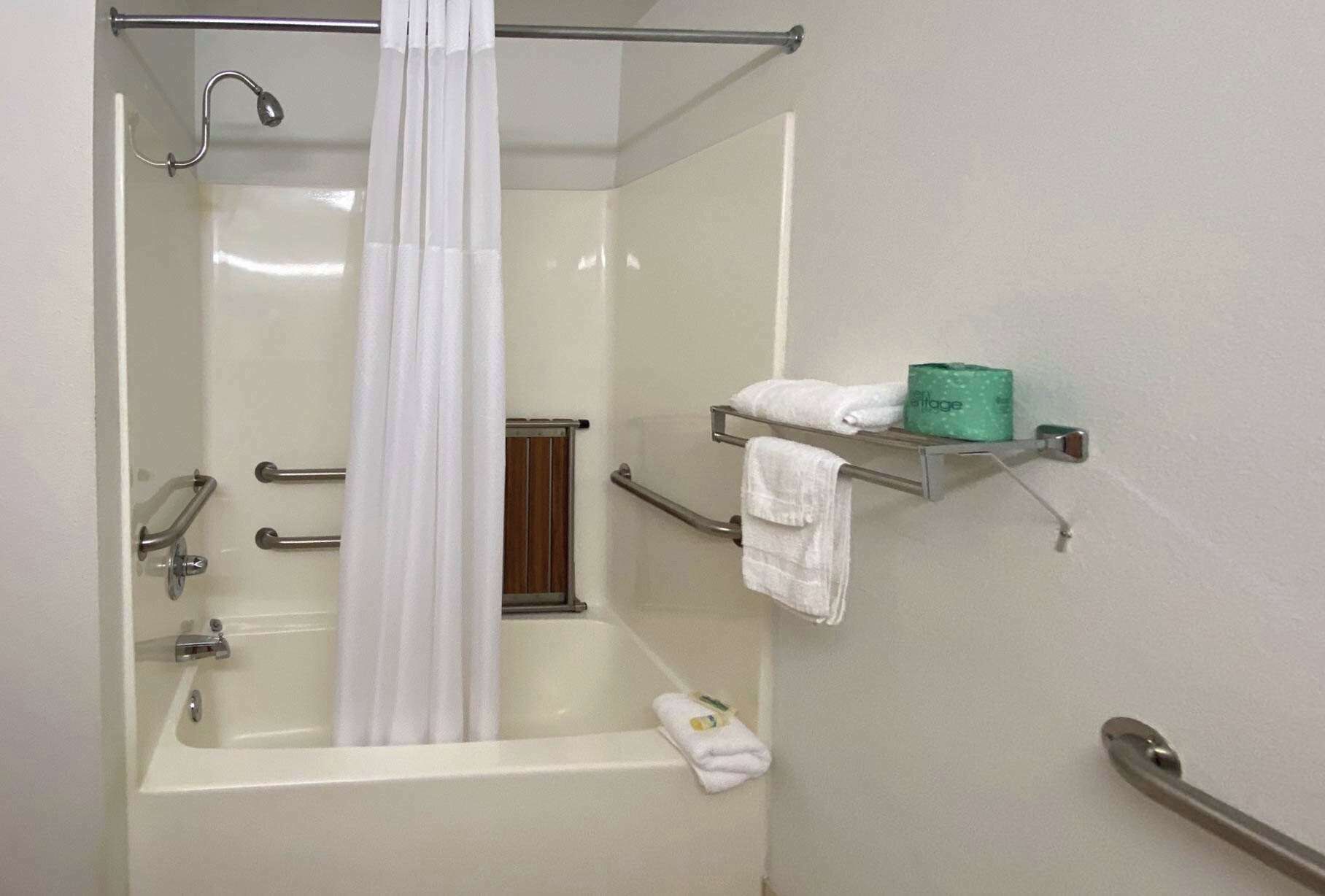 A bathroom with a bathtub, a shower curtain, a towel rack with towels, and a toilet paper holder.