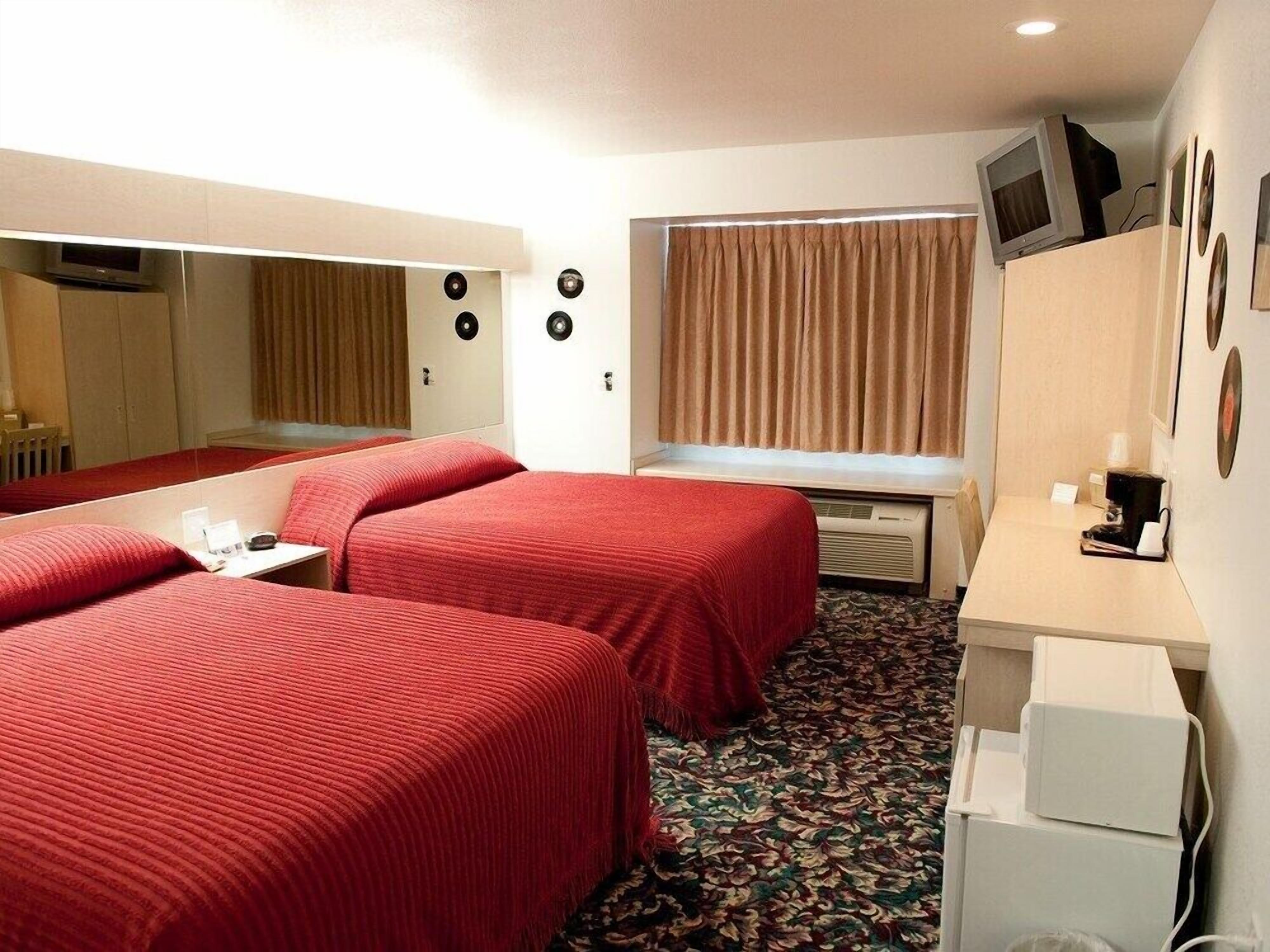 Quarto de hotel com duas camas, uma escrivaninha, televisão e janela com cortinas.