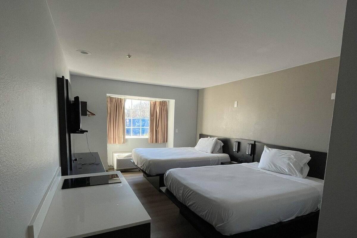 A hotel room with two beds, a desk, a TV, and a window with curtains.