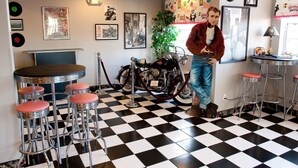 A bar area with checkered flooring, bar stools, a motorcycle, and various framed pictures on the walls. - Motel 6 McAlester, OK - South (McAlester)