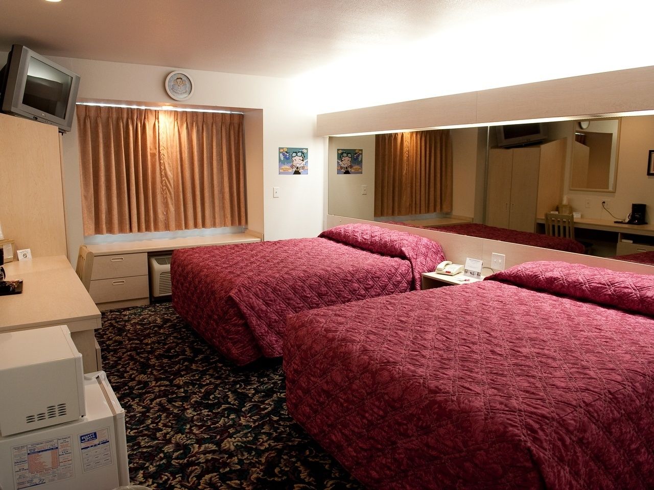 Et hotelværelse med to senge, et skrivebord, et fjernsyn og et spejl.
