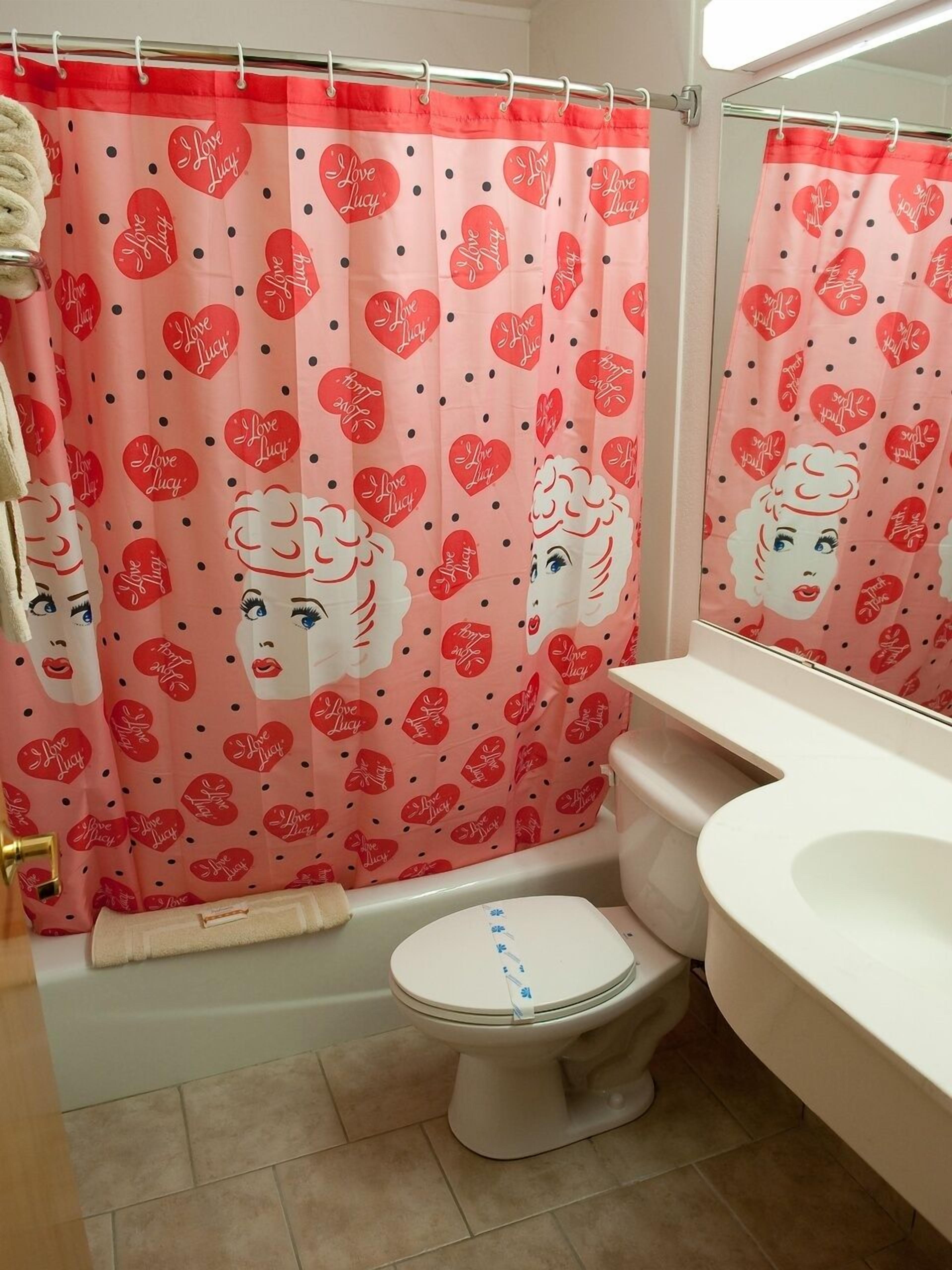 Un baño con inodoro, lavamanos y cortina de ducha con estampado de corazones y un rostro.