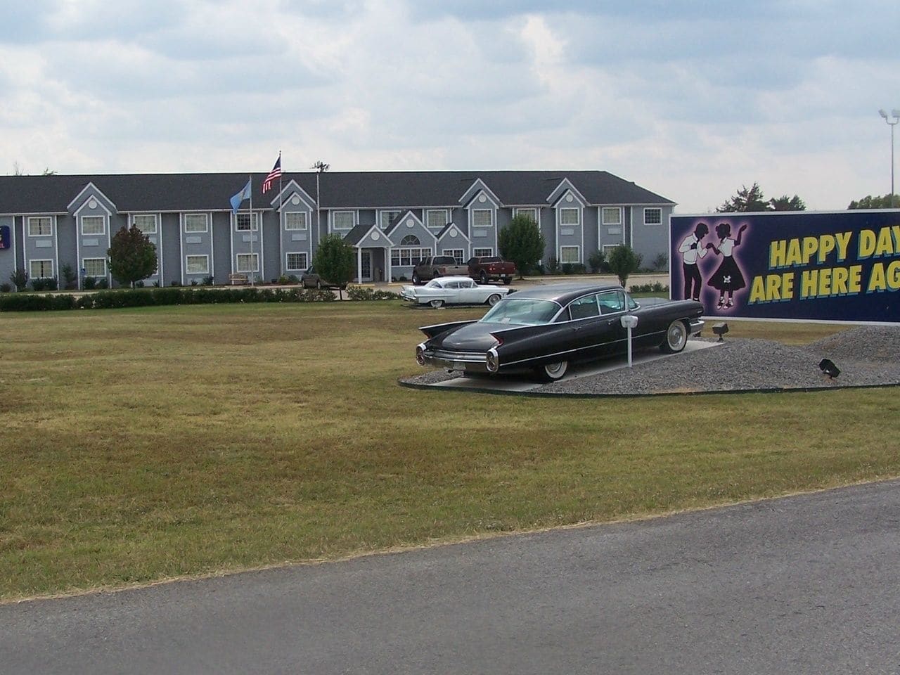 A hotel with a large parking lot, a grassy area, and a billboard with a family illustration.