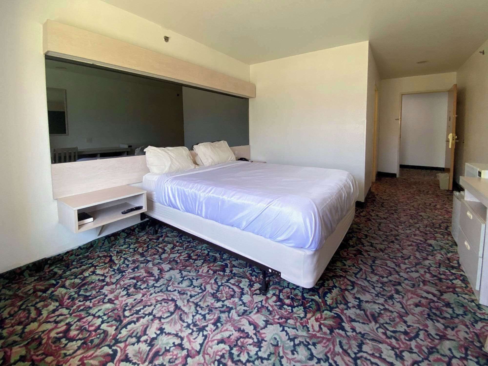 A hotel room with a large bed, a built-in desk, and a patterned carpet.