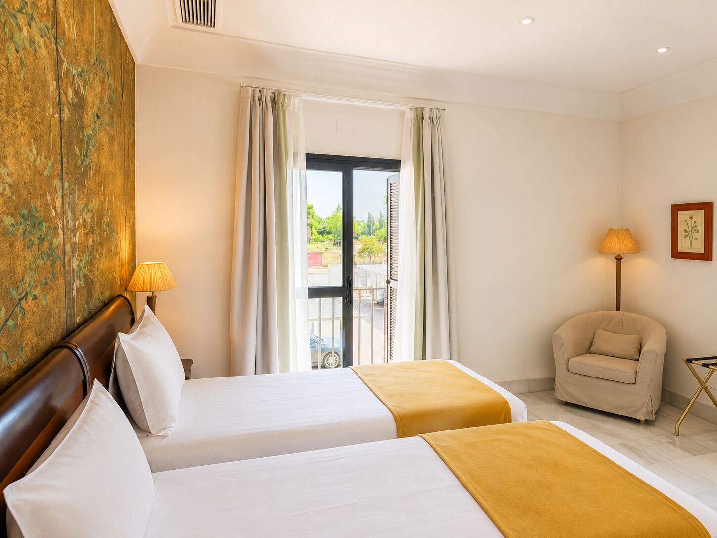 A hotel room with two beds, a chair, a lamp, and a view of the outdoors.