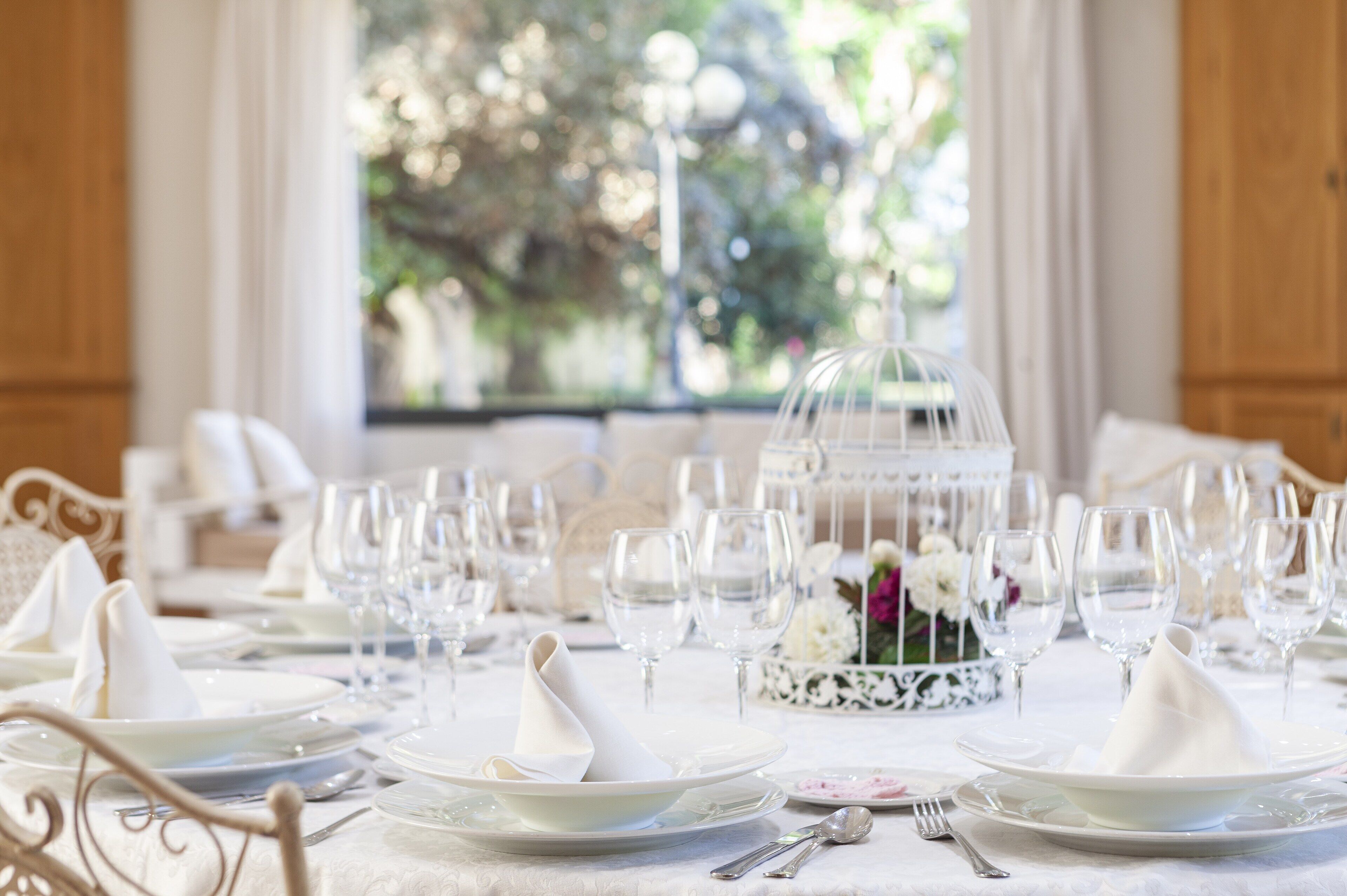 A formal dining table set with white plates, glasses, and silverware, with a decorative centerpiece and a glass dome structure.