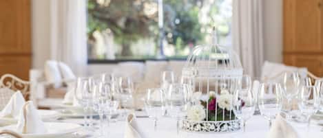 A formal dining table set with white plates, glasses, and silverware, with a decorative centerpiece and a glass dome structure.