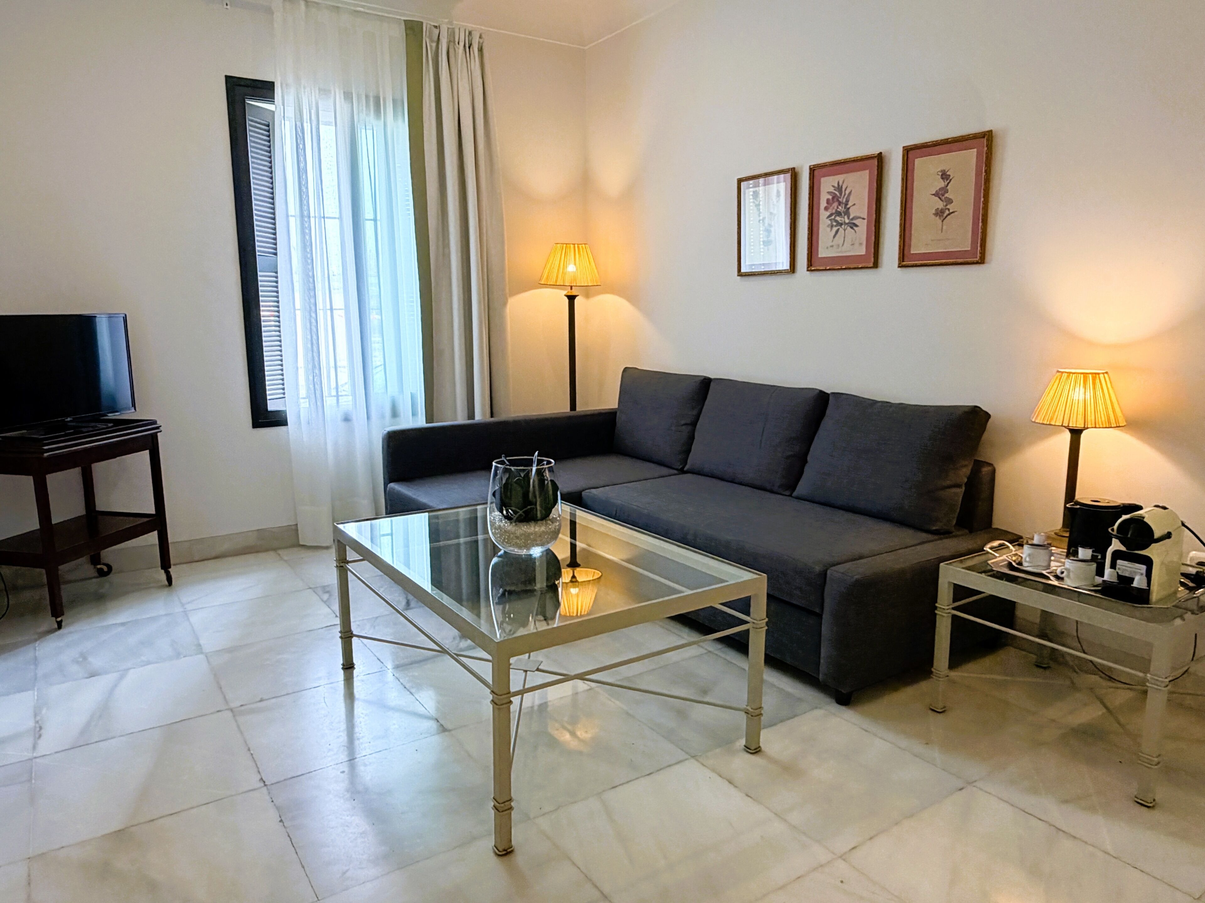 Una sala de estar con un sofá, una mesa de centro de vidrio, un televisor y dos lámparas.