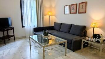 Una sala de estar con un sofá, una mesa de centro de vidrio, un televisor y dos lámparas.