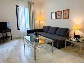 Una sala de estar con un sofá, una mesa de centro de vidrio, un televisor y dos lámparas.